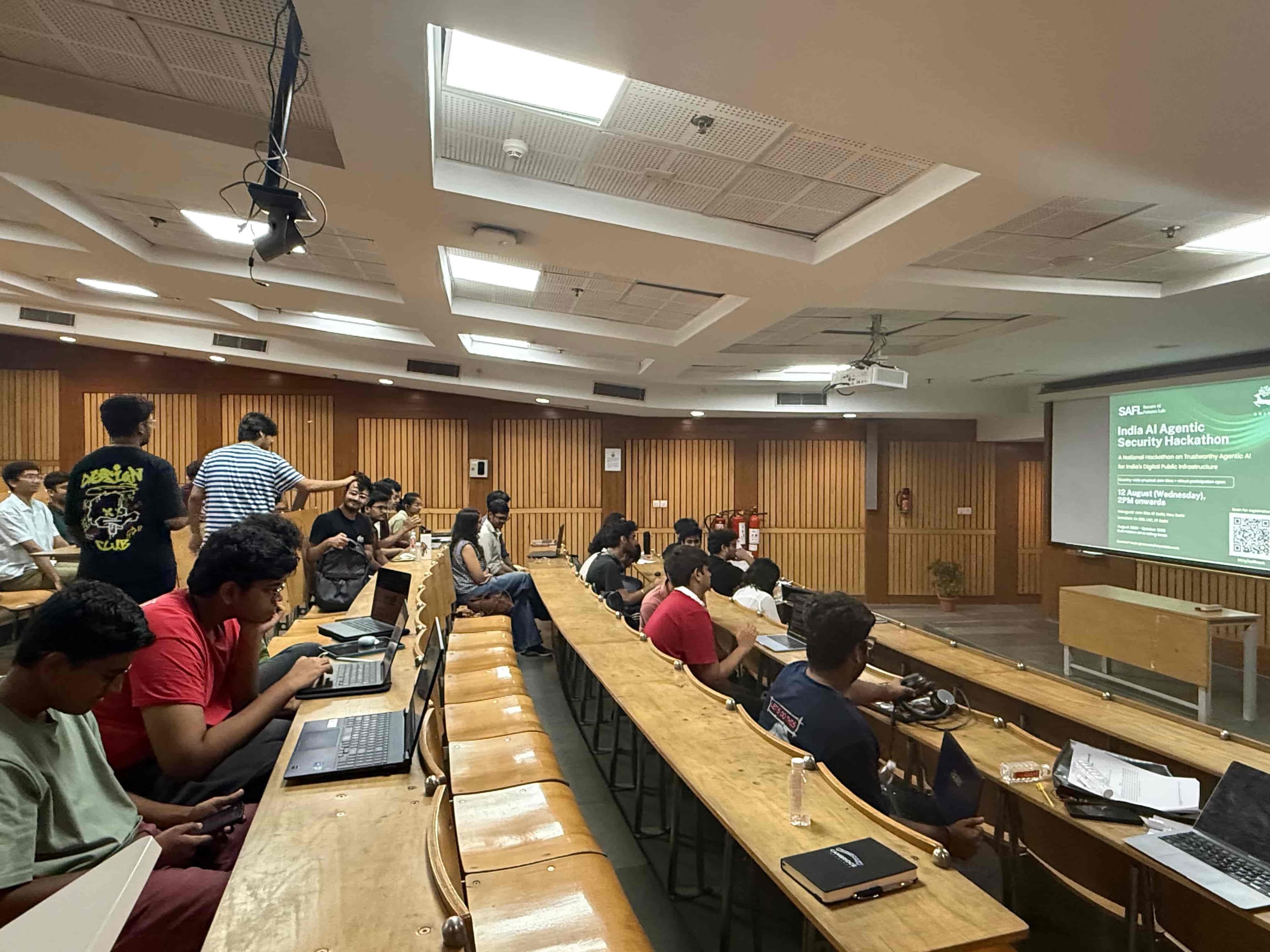 Teams at work on laptops in a lecture hall, with the hackathon title on the projector screen